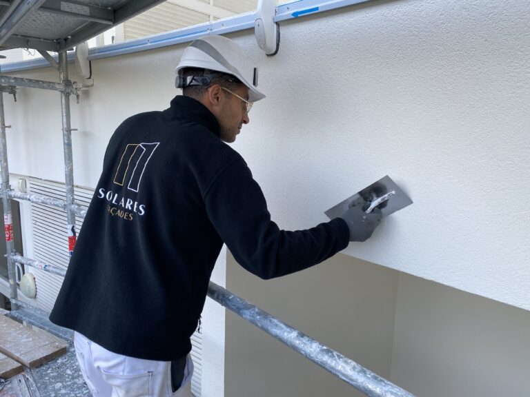 Ouvrier appliquant un RPE sur une façade après le traitement des fissures en façade